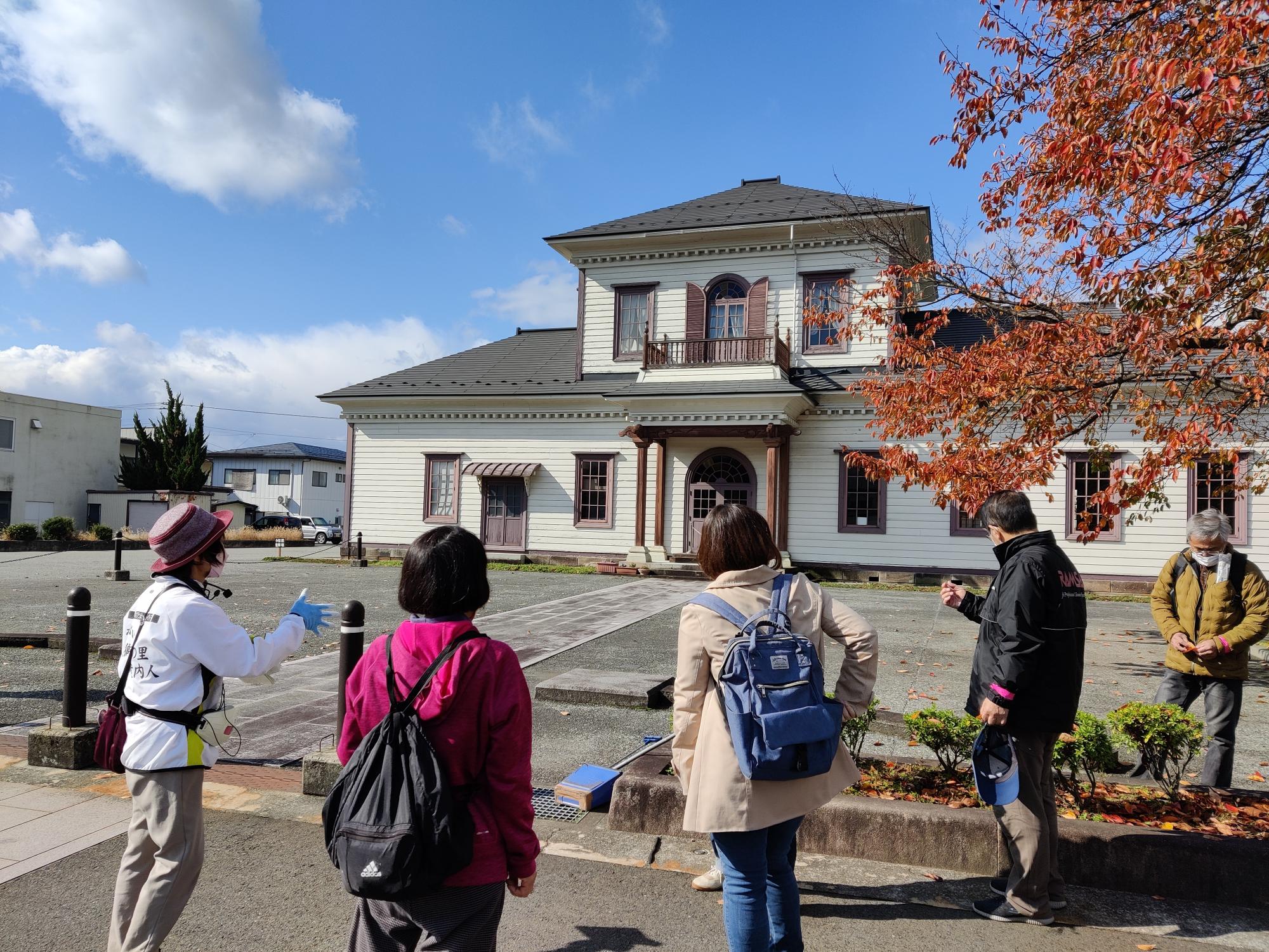 白い外壁で擬洋風建築2階建ての小桜館前に参加者の方々が集まりガイドさんの説明を聞いている様子の写真