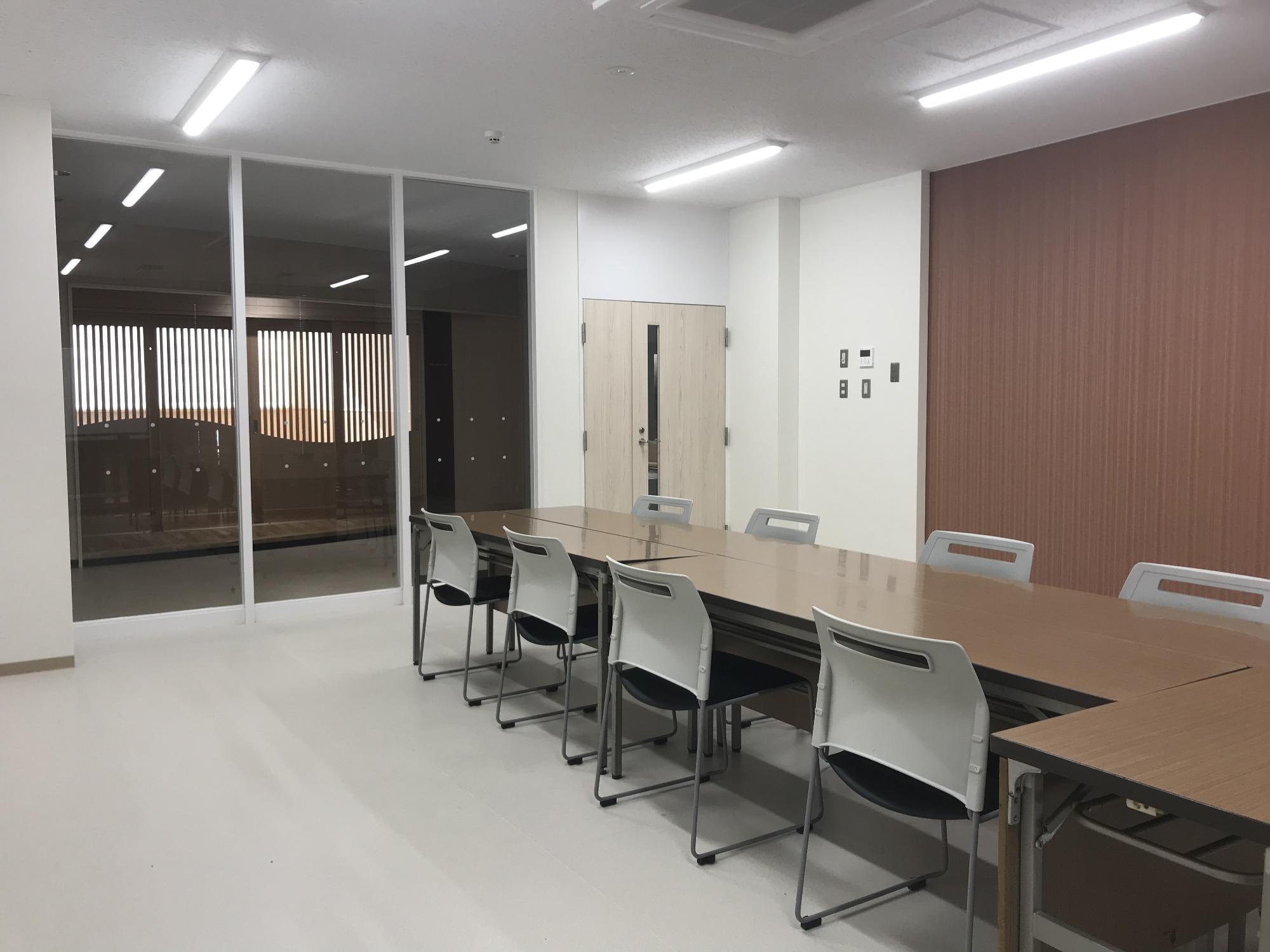 室内右側に長机が置かれ、机左側と右側にそれぞれ4脚ずつ椅子が置かれている会議室1の写真
