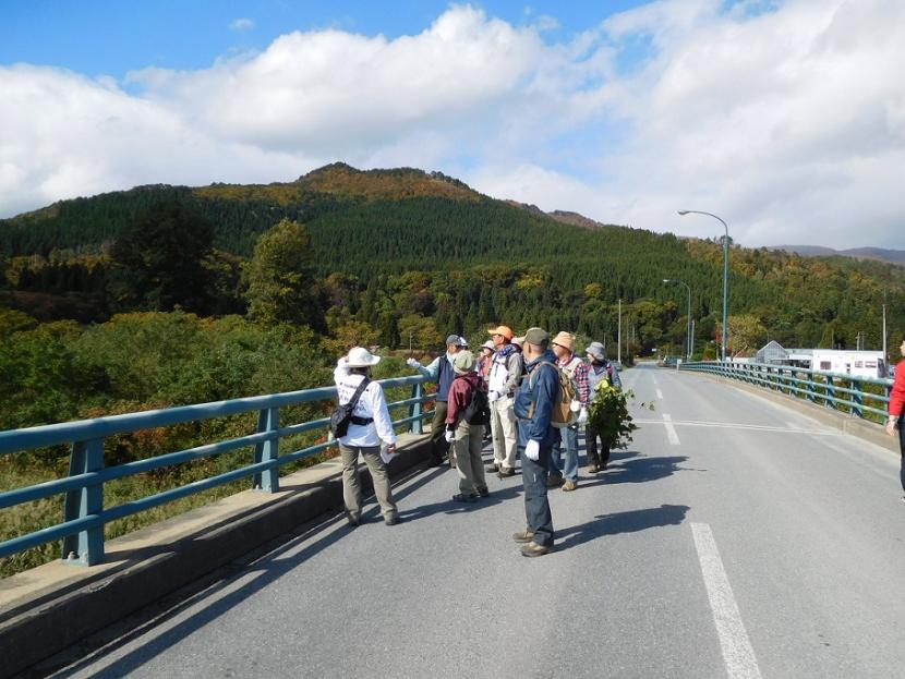 遠くには緑深い山が見え、平泉橋の中央付近に参加者の方々が集まり、ガイドさんの説明を聞いている様子の写真