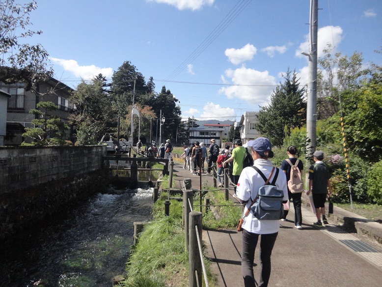 晴天の中、撞木川沿いの遊歩道を参加者の方々が歩きながら散策を楽しんている様子の写真