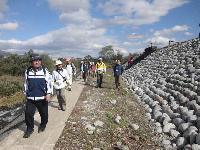 沢山の石が積み上げられて造られた締切堤防が長く続いている側を参加者の方々が歩いている様子の写真