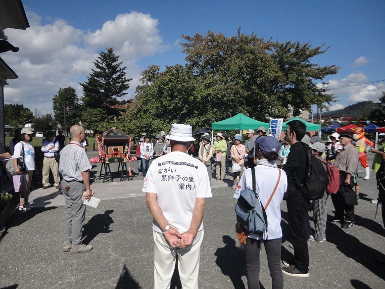 参加者の方々が輪になって集まり、主催関係者と思われる男性の話を聞いている閉会式の様子の写真