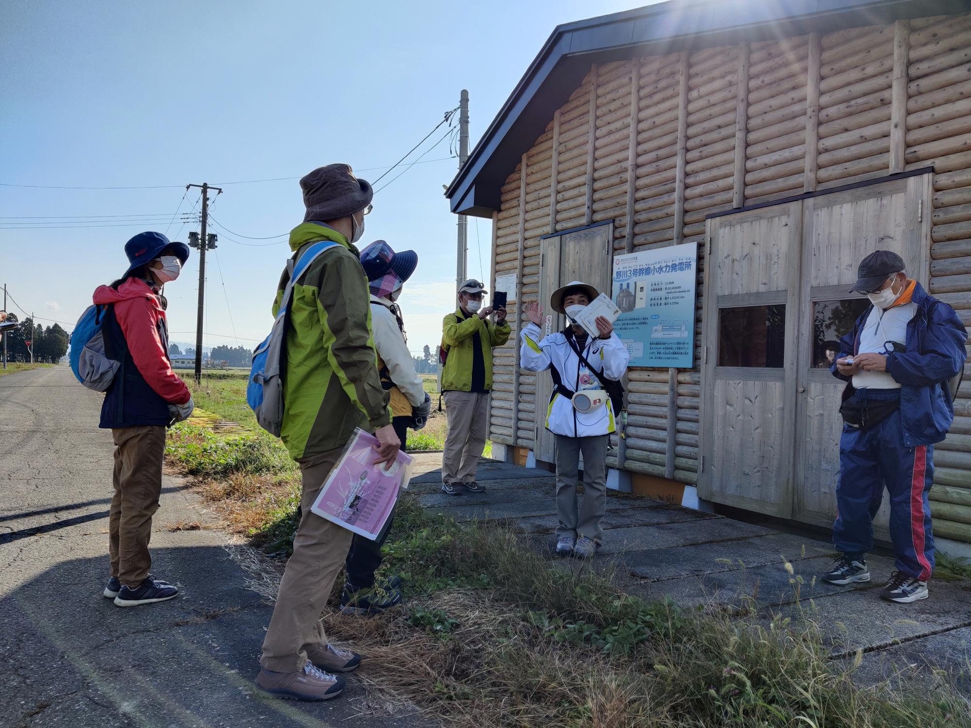 小水力発電所の建物の前で、参加者の方々がガイドさんの説明を聞いている様子の写真