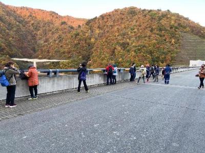 奥には紅葉で色づいた山が見え、ダム堤体上で、遠くを眺めたり、周りを歩いたり、参加者の方々が思い思いに過ごしている自由時間の様子の写真