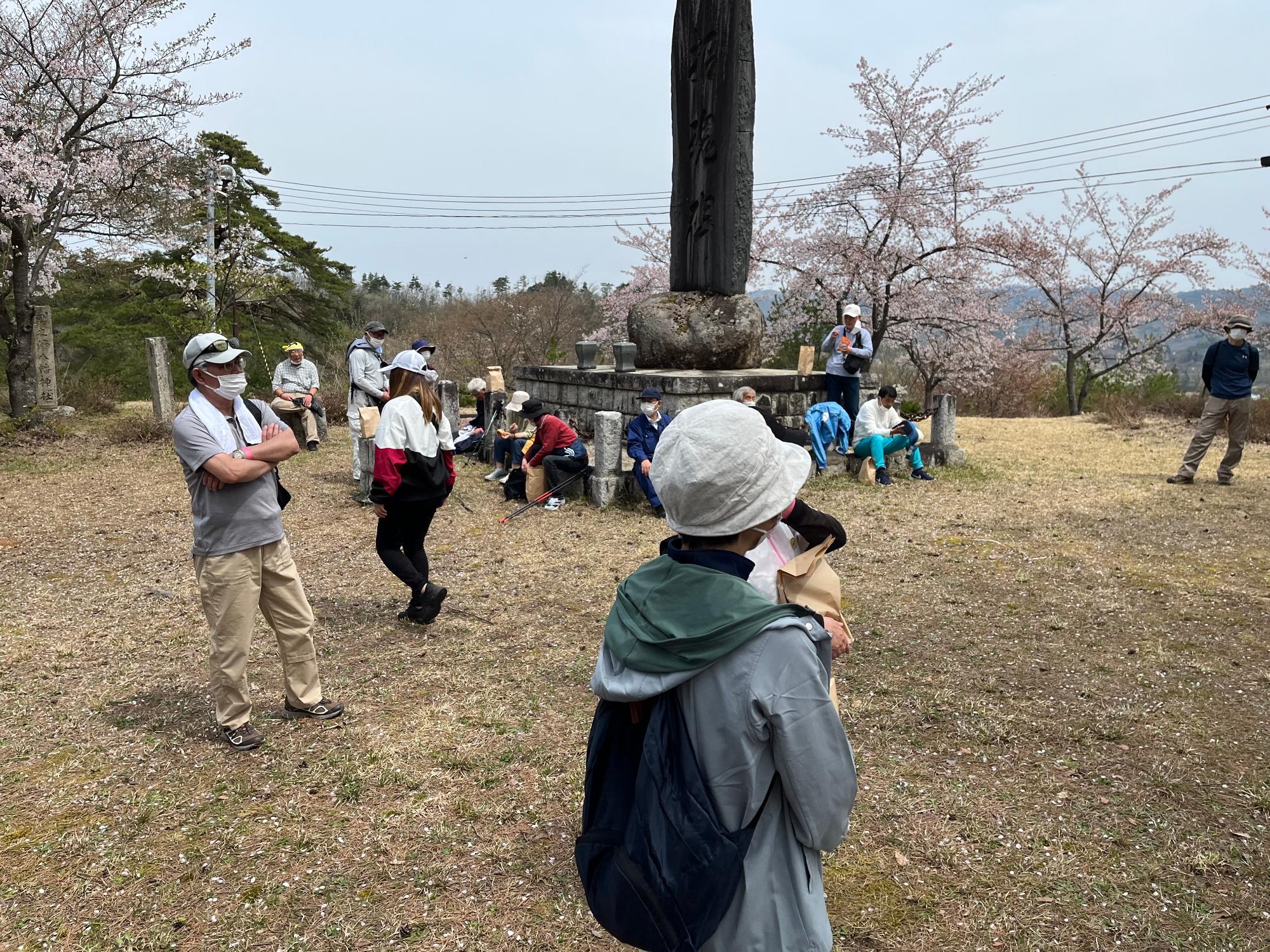 八ヶ森の公園の石碑のある周辺で参加者の方々がおやつタイムで休息をとっている様子の写真