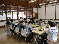 旧長井小学校第一校舎内のテーブルの席に着き、参加者の方々がお弁当を食べている昼食会場の様子の写真