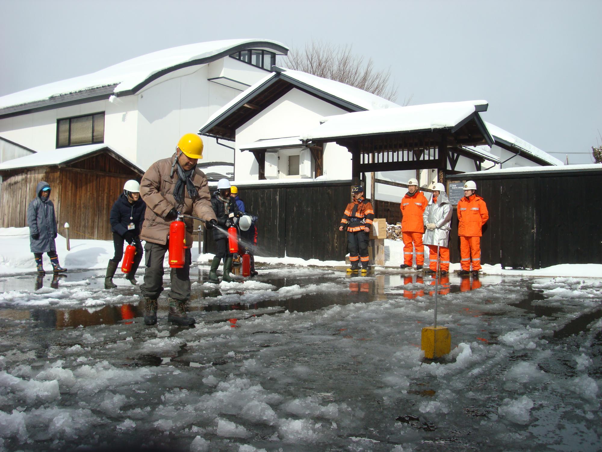 水消火器を持った男性が、地面に置かれた四角い箱のような物に向かって水をかけている消火訓練の様子写真