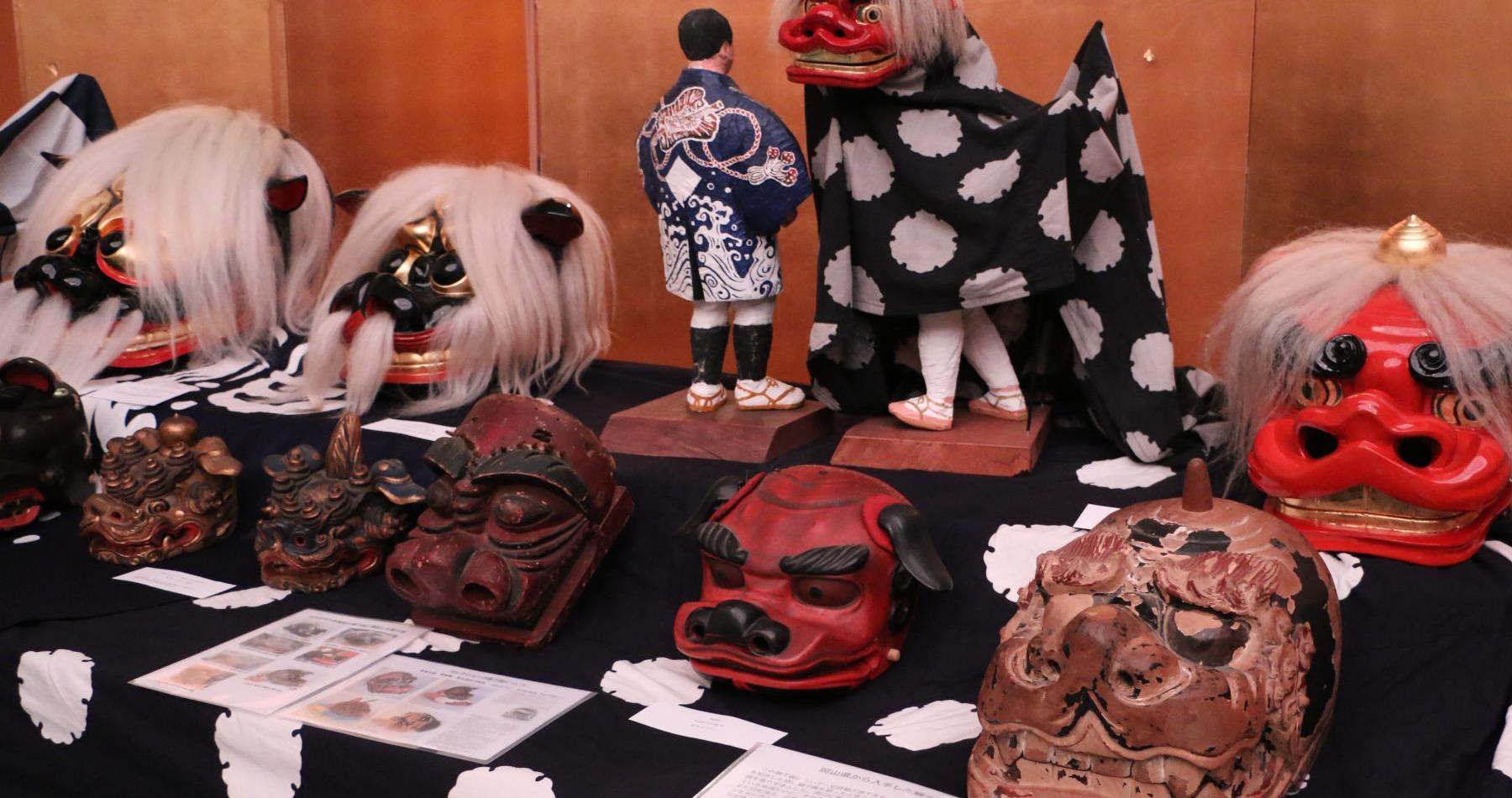 黒い布が敷かれた台の上に様々な獅子舞のお面が展示されている写真